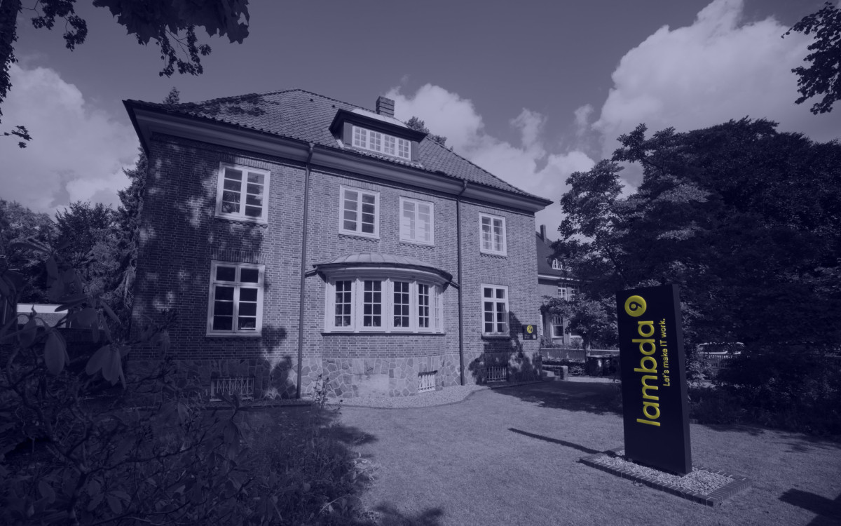 Frontansicht einer Villa im Grünen. Neben der Villa steht ein Leuchtschild mit dem Text „lambda9“.