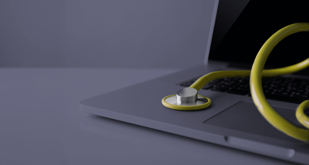 Ein gelbes Stethoskop liegt auf einem Laptop auf.